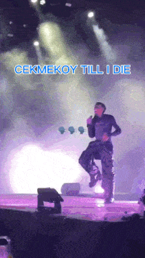 a man singing into a microphone on a stage with the words cekmekoy till i die above him