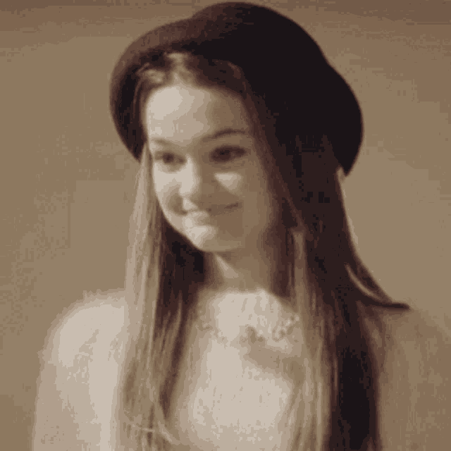 a woman wearing a hat and a white sweater is smiling