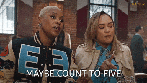 two women are sitting at a table and one of them is wearing a jacket with the letter e on it
