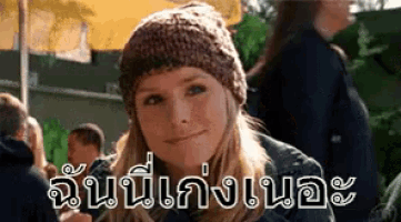 a woman wearing a knitted hat is smiling in front of a group of people in a foreign language .