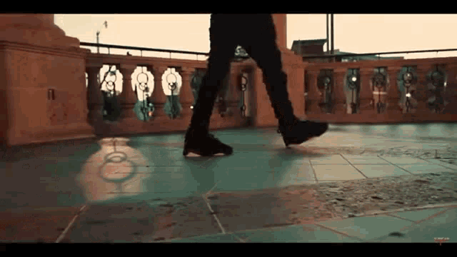 a person is walking on a tiled floor in front of a balcony .
