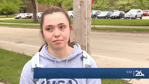a woman wearing a sweatshirt that says ucsd stands in front of a parking lot