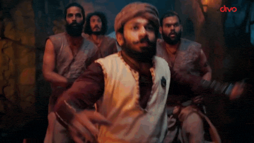 a man with a beard is standing in front of a group of men and says wait what ?