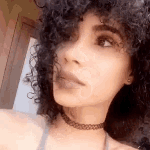 a woman with curly hair is wearing a choker necklace and earrings .
