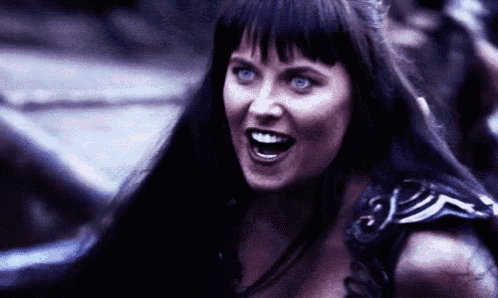 a woman with long black hair and blue eyes is smiling and making a funny face .