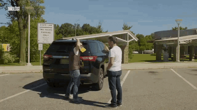 two men standing in front of a state law two hour parking only sign
