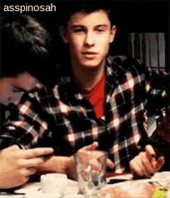 a man in a plaid shirt sits at a table with a glass of water