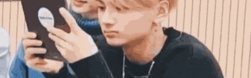 a young man is looking at a cell phone while wearing headphones and a black shirt .