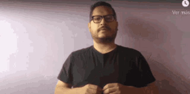 a man with glasses and a beard is wearing a black shirt against a purple wall .