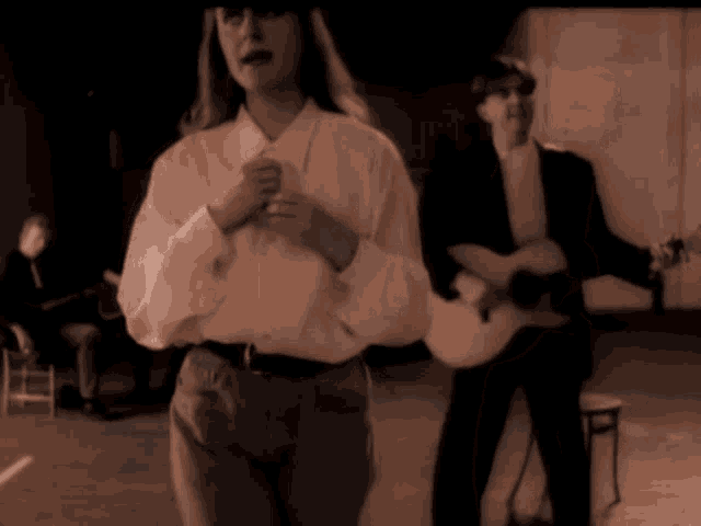 a woman in a white shirt is standing in front of a man playing a guitar