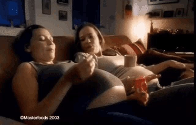 two pregnant women are sitting on a couch in a living room .