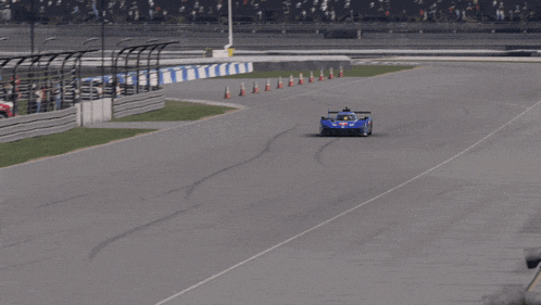 a race car is driving down a track with a shadow of a fence in the background