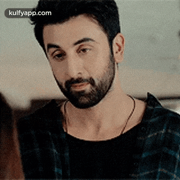 a man with a beard is looking at something while wearing a plaid shirt and a black shirt .