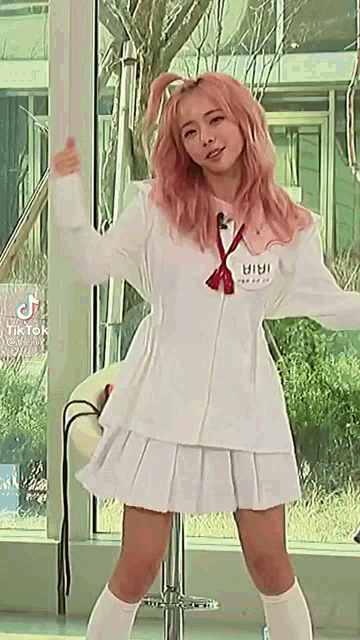 a woman in a white dress and pink hair is standing in front of a window .