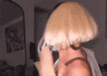 a woman wearing a blonde wig is talking on a cell phone in front of a mirror .