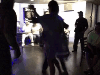 a group of people are dancing in a dark room with a dart board on the wall