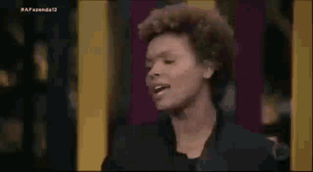 a woman with curly hair is making a funny face while standing in front of a yellow and purple wall .