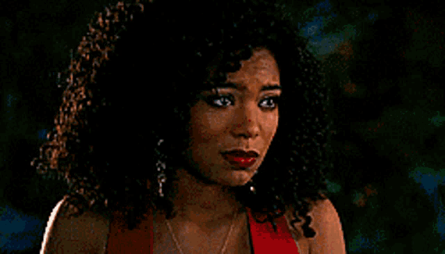 a woman with curly hair is wearing a red dress and necklace .