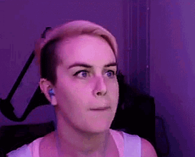 a woman with a shaved head is making a funny face in front of a purple background .