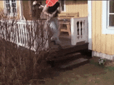 a woman is standing on the porch of a yellow house with a red heart in the background