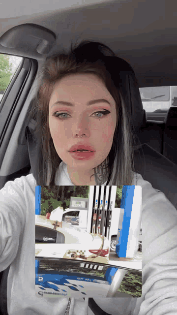 a woman is sitting in a car holding a picture of a gas pump