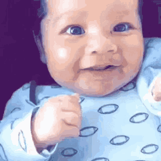 a baby in a blue shirt is smiling and making a fist in the air .