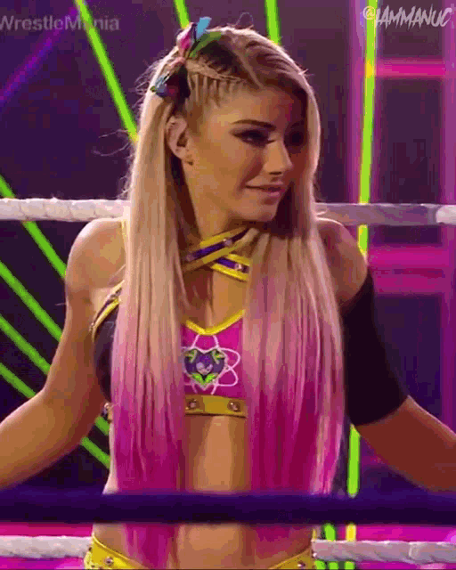 a female wrestler with pink hair is standing in a wrestling ring .