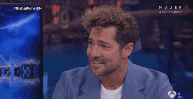 a man with curly hair is smiling in front of a screen that says mujer a continuacion