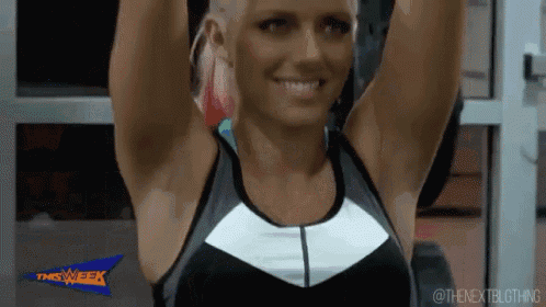 a woman is smiling and lifting her arms in a gym while wearing a nike tank top .