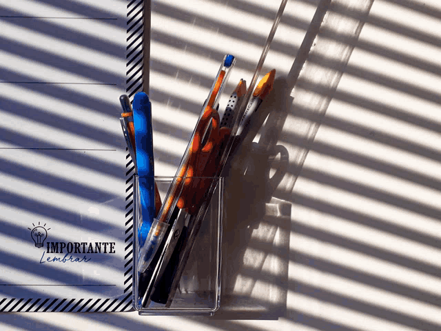 a container of pens sits next to a notepad that says " importante " on it