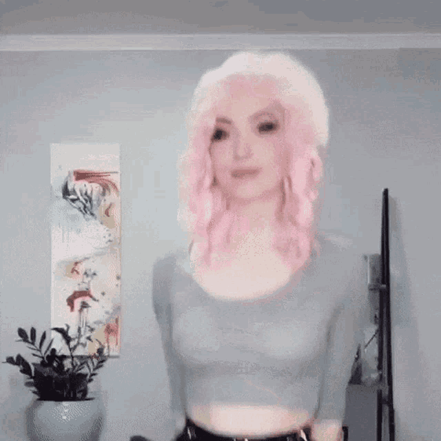 a woman with pink hair is standing in a room wearing a crop top and black skirt .