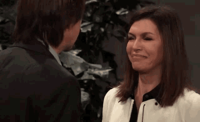 a man and a woman are looking at each other and smiling . the woman is wearing a white jacket .