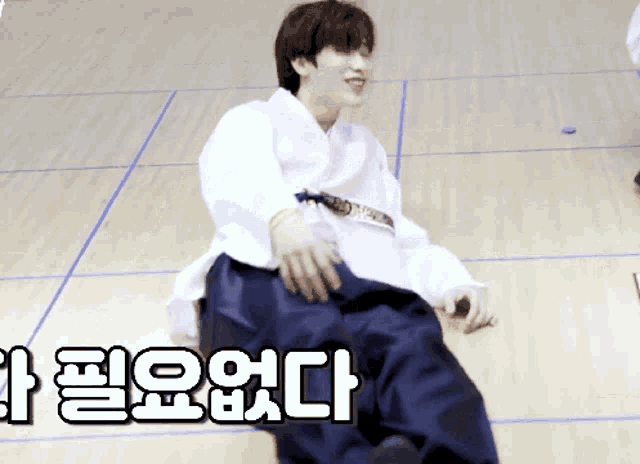 a man in a white shirt and blue pants is sitting on a wooden floor with korean writing on the floor behind him