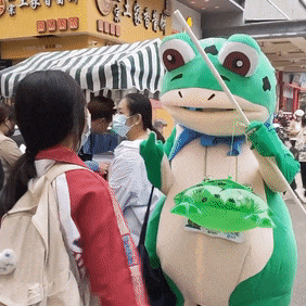 a green frog mascot is holding a stick and a green bag