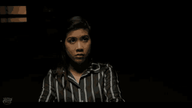 a woman in a striped shirt is making a funny face in a dark room .