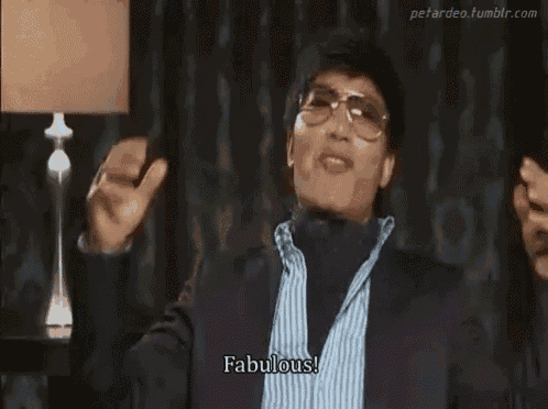 a man wearing glasses and a turtleneck is holding a cell phone and says fabulous .