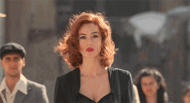 a woman with red hair and red lipstick stands in a crowd of people
