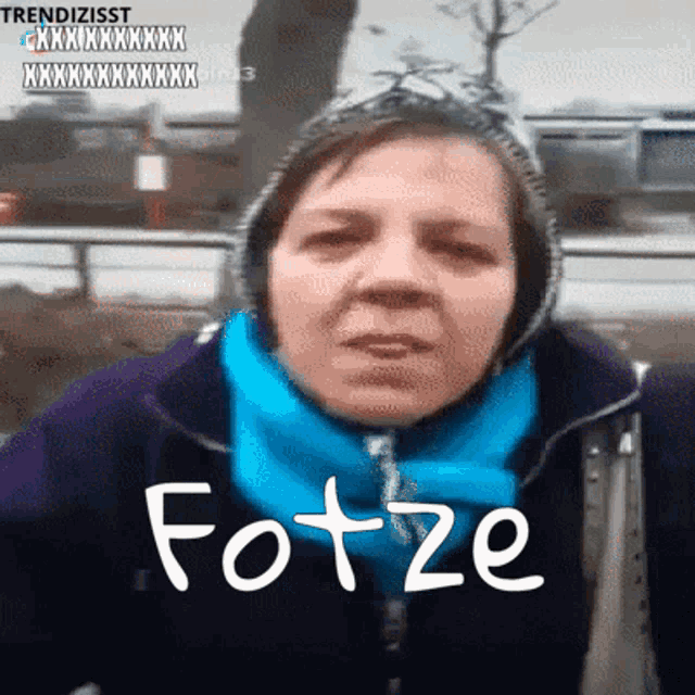 a woman wearing a hooded jacket and a blue scarf has the word fotze written on her face