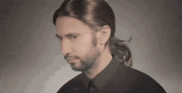 a man with a ponytail and a beard wearing a black shirt and tie .