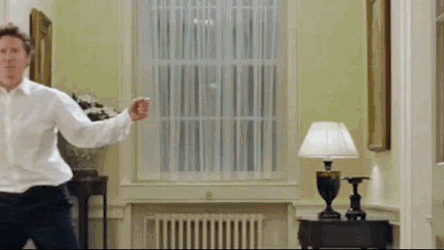 a man in a white shirt is standing in a room with a lamp