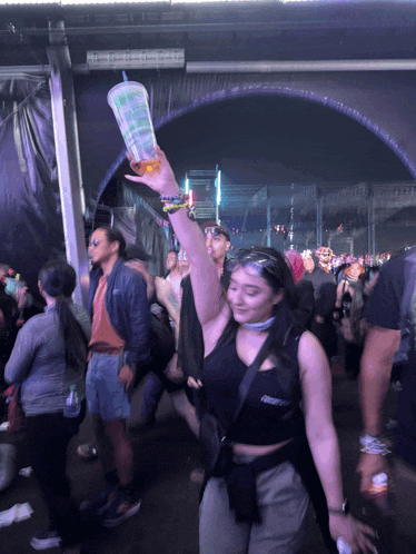 a woman holds up a cup with a straw that says ' iced tea ' on it in a crowd of people