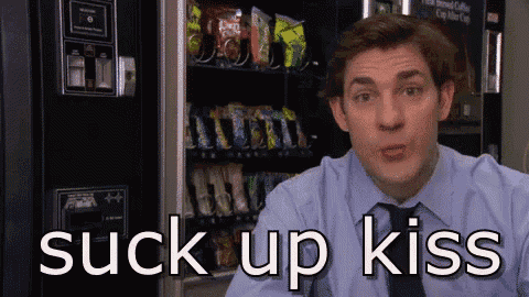 a man in a suit and tie is sitting in front of a vending machine that says " suck up kiss " .