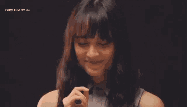 a woman is smiling with her eyes closed and holding a cell phone in her hand .