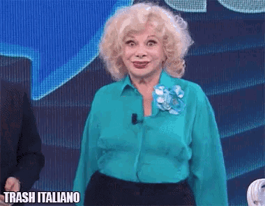 a woman wearing a blue shirt with a flower on her collar is standing in front of a screen that says trash italiano on it