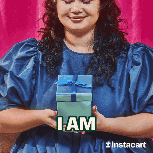 a woman in a blue dress is holding a gift box with the word i am above it