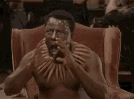 a shirtless man is sitting in a chair wearing a necklace and making a face .