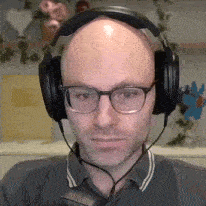a bald man with glasses and headphones is looking at the camera .