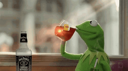 a kermit the frog is drinking a cup of tea next to a bottle of jack daniel 's whiskey .