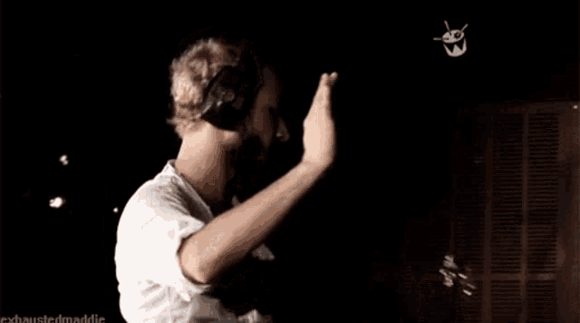 a man wearing headphones is dancing in a dark room with a drawing of a face on the wall behind him .
