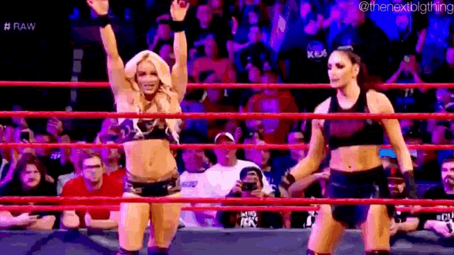 two female wrestlers are standing in a wrestling ring with their hands in the air .